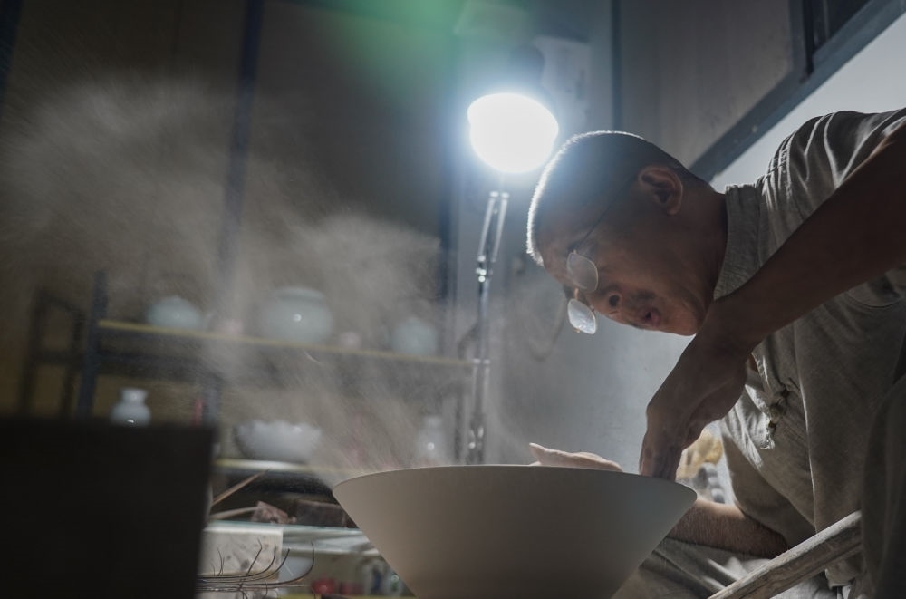 ↑ 在景德鎮(zhèn)，手工匠人吹去坯內(nèi)的泥土（2021年7月14日攝）。