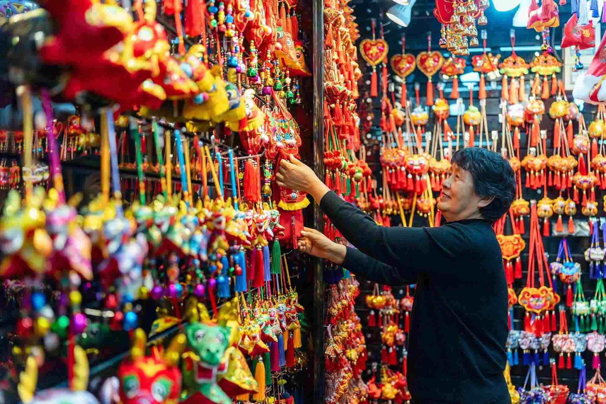 2023年12月11日，金華義烏國際商貿(mào)城，龍年喜慶用品掛滿攤位，顧客正在挑選中。