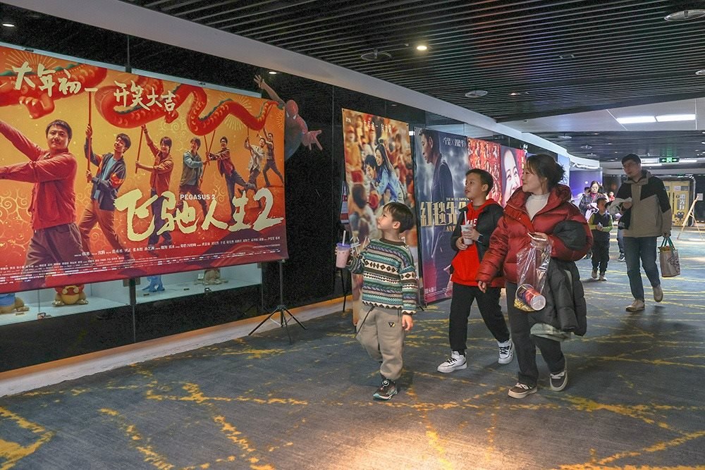 △ 2024年2月16日，在江西贛州一家電影院，觀眾從春節(jié)檔電影的宣傳展板前走過(guò)。