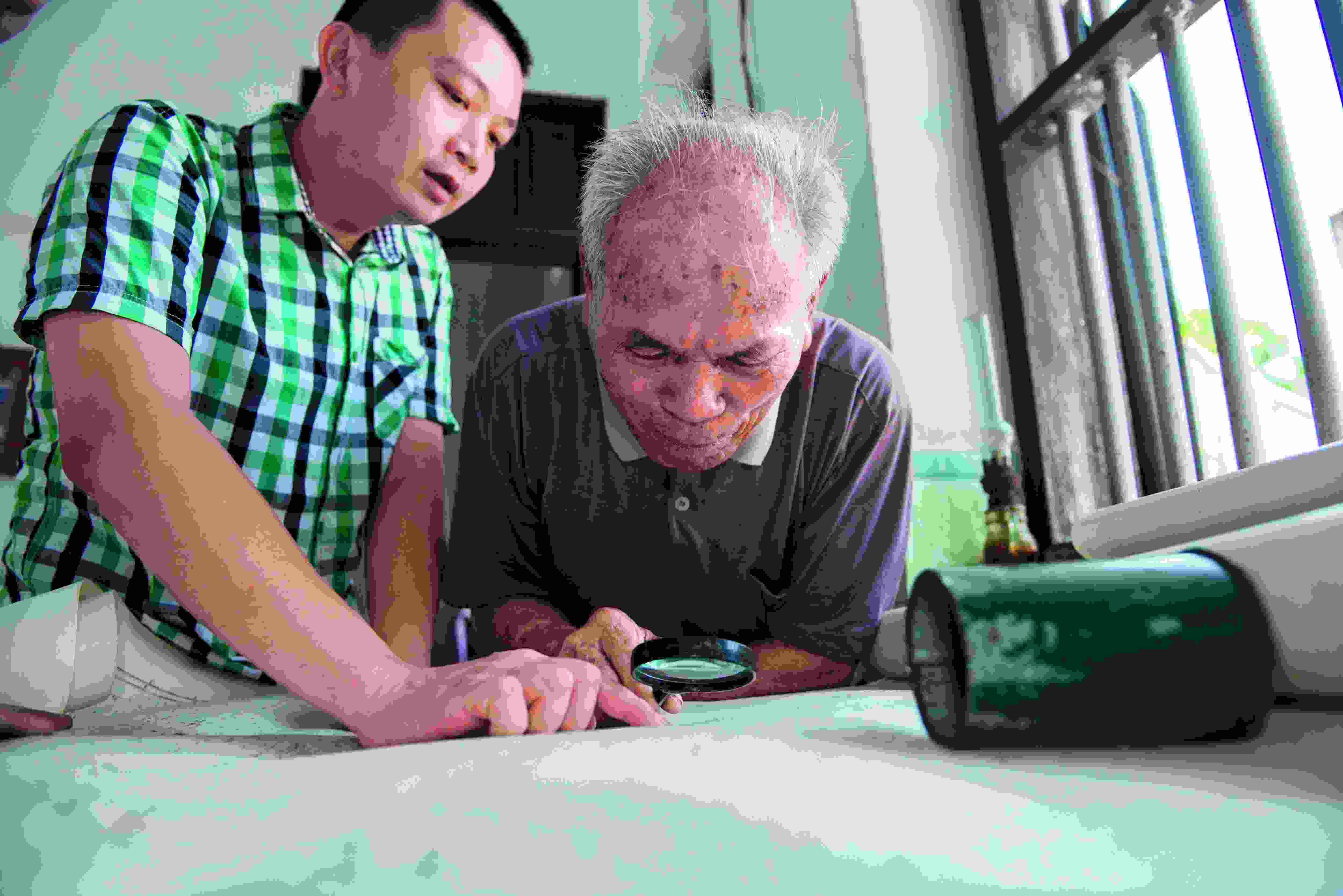 2016年6月14日，海南草塘村89歲的老船長(zhǎng)盧業(yè)發(fā)（右）向他的兒子傳授《更路簿》的使用方法。