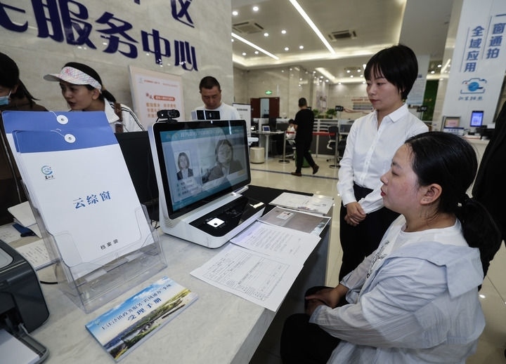 在浙江省嘉興市秀洲區(qū)王江涇鎮(zhèn)便民服務(wù)中心的“跨域通辦·云綜窗”窗口，辦理開業(yè)登記的個(gè)體工商戶（右一）通過(guò)該系統(tǒng)與江蘇省蘇州市吳江區(qū)盛澤鎮(zhèn)行政審批局工作人員視頻連線，進(jìn)行身份讀取及材料線上審核（2024年5月9日攝）。新華社記者 徐昱 攝