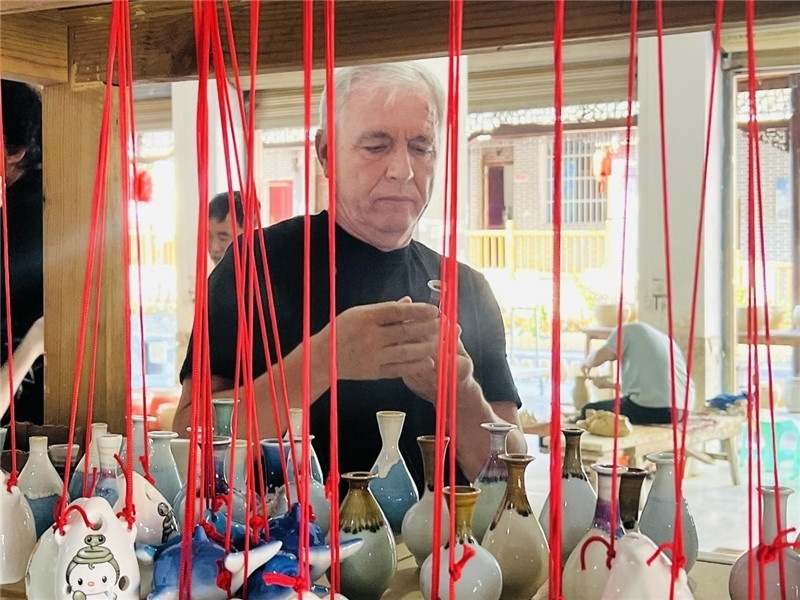鄉(xiāng)愁如同一根根紅線，將游子與故鄉(xiāng)永遠(yuǎn)地牽連到一起?；逄账囄幕瘎?chuàng)意一條街的母氏陶藝館內(nèi)，紅線吊著陶瓶，思緒游走萬里。摩爾多瓦“信息標(biāo)簽”通訊社社長亞歷山大·塔納斯端詳著館內(nèi)展示的陶藝作品，并挑選出心儀的小擺件帶回摩爾多瓦，也帶走花茂村的“鄉(xiāng)愁”。（張亞欣攝）