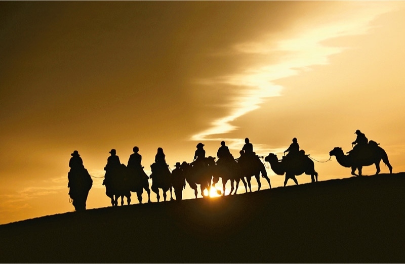 新時(shí)代以來(lái)，文化和旅游深度融合發(fā)展體制機(jī)制不斷健全，成功走出了一條獨(dú)具特色的中國(guó)旅游發(fā)展之路。圖為2024年9月1日清晨，游客在甘肅省敦煌市鳴沙山月牙泉景區(qū)乘騎駱駝，欣賞大漠風(fēng)光，體驗(yàn)絲路風(fēng)情。 新華社發(fā) 張曉亮/攝