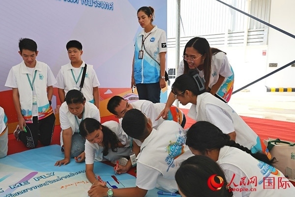 泰國學(xué)生在開營儀式展板上繪制圖案。人民網(wǎng)記者 白元琪攝
