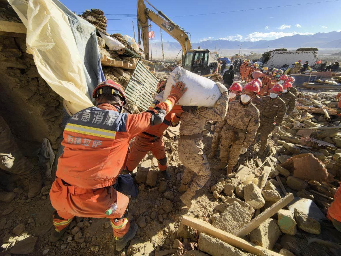 1月11日，定日縣長所鄉(xiāng)古榮村，應急消防等救援人員排隊接力搶運掩埋在倒塌房屋下的群眾財物。人民日報記者楊翹楚攝