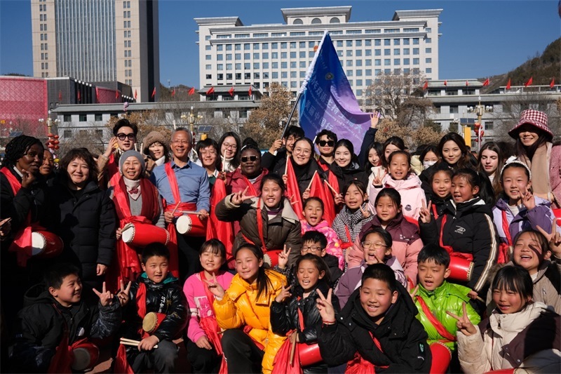 中外青年學子在安塞文化廣場觀看陜北腰鼓和大秧歌表演后合影留念，大家踏著鼓點共舞，翻飛的紅綢與躍動的身影交織，在黃土地廣場上繪出一幅生動的陜北民俗互動畫卷